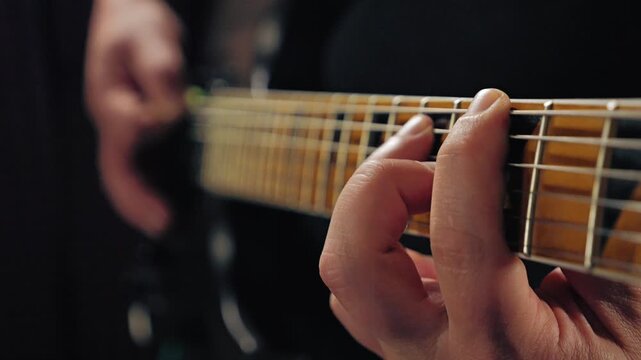 Close-up of a hand pressing the strings of an electric guitar. Perspective view from the neck. Slow motion footage of an electric guitar player playing in a recording studio