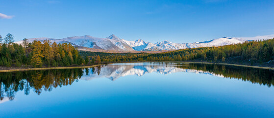 Calm alpine lake reflects snow covered peaks and fall forest along quiet shore creating serene winter landscape