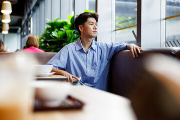 Young man gazes out window in restaurant booth.