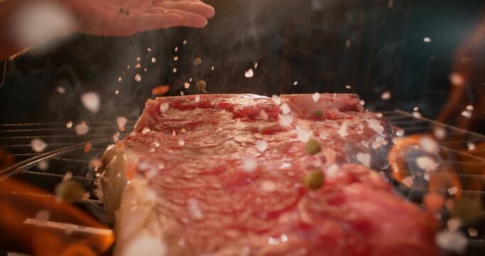 Delicious cinematic food scene: chef seasoning and grilling a juicy t-bone steak on a fiery barbecue grill in slow motion. Great for commercials, restaurant promos, and cooking videos