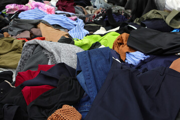 pile of numerous used garments clothing and attire on an outdoor flea market stall