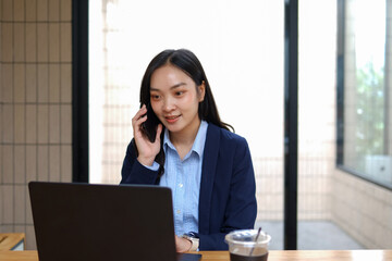 Businesswoman talking on mobile phone and using laptop in office with determination.