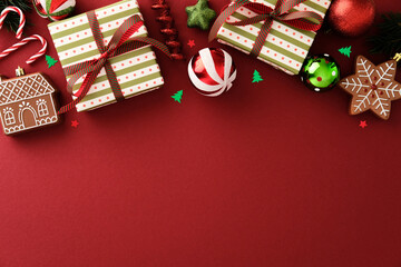 Christmas flat lay with gifts, gingerbread cookies, baubles, candy canes, and confetti on red background. Space below for text, ideal for festive promotions or greeting cards.