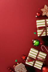 Christmas flat lay with gifts, gingerbread cookies, ornaments, candy cane, pine branches, and confetti on red background. Top view, vertical