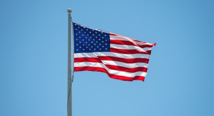 Obraz premium American flag waving in the wind against a clear blue sky on a sunny day