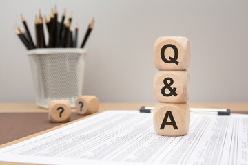 wooden cubes stacked with Q and A letters on office desk with financial papers.