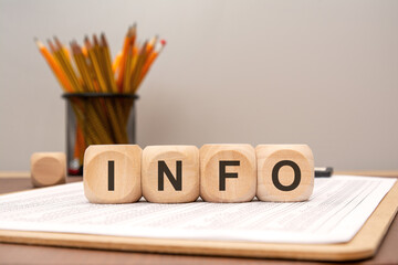 Wooden blocks forming word INFO on office desk with financial documents and pencils.