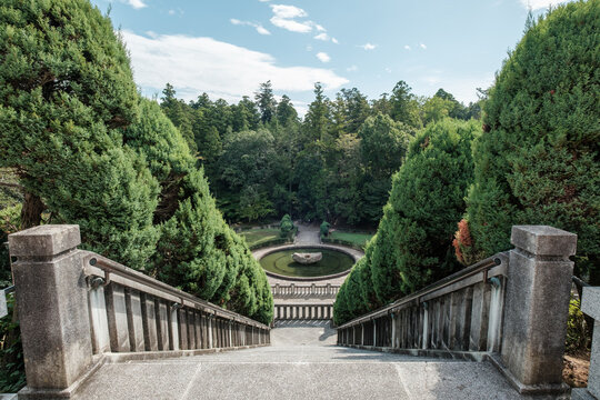 View of the stone staircase leading down to a tranquil pond surrounded by lush greenery and trees, creating a serene atmosphere, Narita, Chiba, Japan.