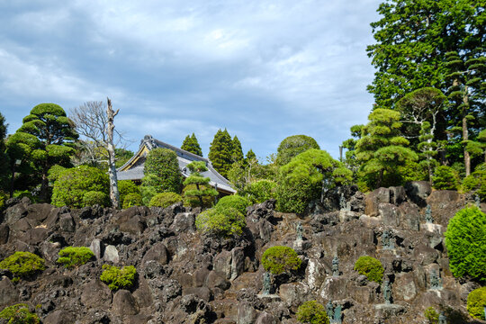 View of a serene Japanese garden with meticulously pruned trees and weathered stone statues, a temple roof peeking through, Narita, Chiba, Japan.