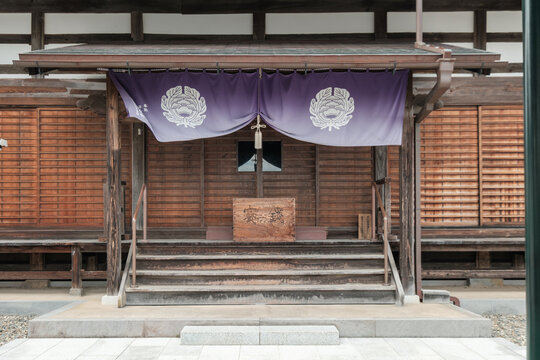 View of an ornate temple entrance featuring wooden steps, a purple curtain with emblems, and intricate details, Narita, Chiba, Japan.