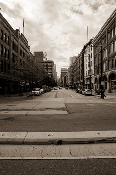 View of sepia-toned buildings line a quiet street with parked cars under a cloudy sky, captured in a ground-level perspective, Denver, Colorado, United States.