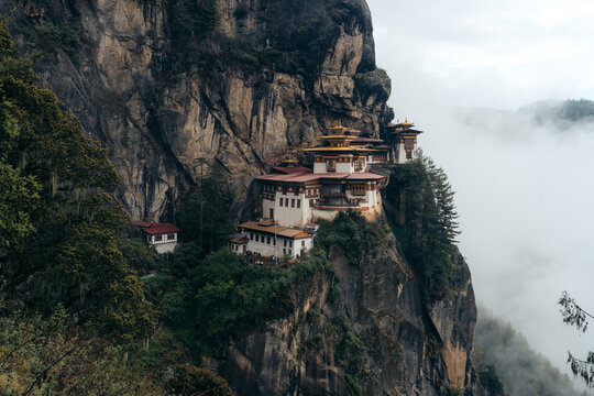 View of the Tiger's Nest monastery clinging dramatically to a sheer cliff face amidst swirling mists, a testament to faith and architectural wonder, Paro, Bhutan.