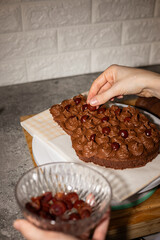 Hands of a woman pastry chef adding cherry into a chocolate cake.