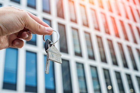 Keys to the Future: Unlocking Opportunities in the Modern City. Symbolic image of a hand holding keys with a blurred futuristic glass building in the background - Powered by Adobe