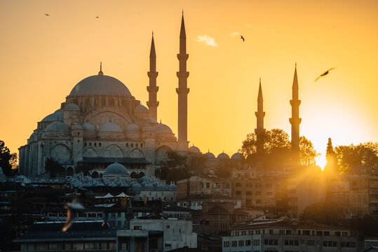 View of a majestic mosque silhouetted against a fiery sunset, its towering minarets piercing the golden sky above the bustling city, Istanbul, &Auml;&deg;stanbul, T&Atilde;&frac14;rkiye.