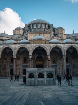 View of an ancient mosque with a grand dome, arched colonnades, and people walking in its expansive courtyard, Istanbul, &Auml;&deg;stanbul, T&Atilde;&frac14;rkiye.
