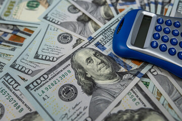 Close-up of US 100 dollar bills with a blue calculator, symbolizing financial planning.