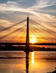 Obraz premium Silhouette of a cable-stayed bridge at sunset over a river (1)