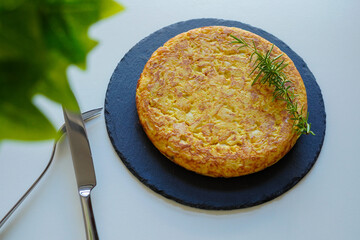 Homemade Spanish omelette (tortilla de patatas) with fork and knife on a white table 