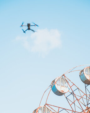 View of a drone hovering above a weathered Ferris wheel against a pale blue sky, capturing the essence of a bygone era, Osaki, Miyagi, Japan.