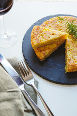 Homemade Spanish omelette (tortilla de patatas) placed on a black plate and a glass of red wine