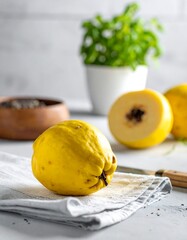 A bright yellow quince rests on a linen cloth, with a sliced quince and herbs visible in the background