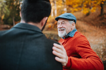 Grandad and grandson sitting on bench in park and hugging.