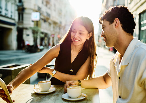 Young couple enjoying conversation and coffee together and taking a selfie with a smartphone at an outdoor urban cafe table - Powered by Adobe