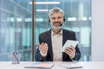 Senior businessman wearing headset holding tablet having video call