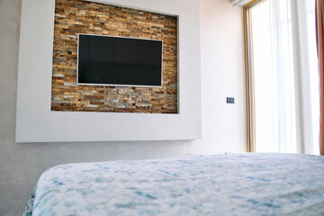 Modern Bedroom Design Featuring a Stylish Wall-Mounted TV with Stone Accent and Cozy Bedding Enhancing the Relaxing Ambiance of the Space