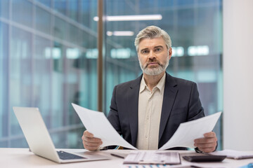 Fototapeta premium Senior businessman reviewing documents in modern office