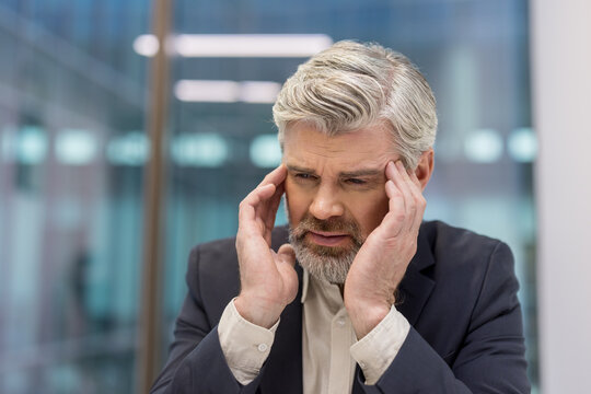 Senior businessman experiencing headache, suffering from stress and burnout