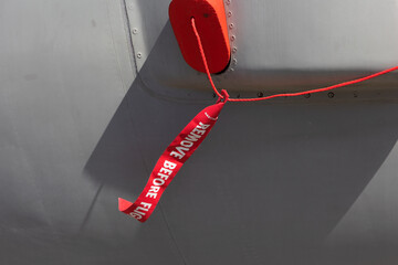 Remove before flight - safety warnign red ribbon and tag. Detail of airplane, plane. Safety procedure in aviation and aeronautics.