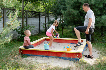 Father enjoys quality time with his children while playing in a sandbox in a backyard