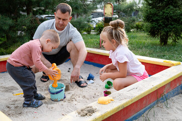 Father enjoys a fun day outdoors playing in the sand with his young children in the park