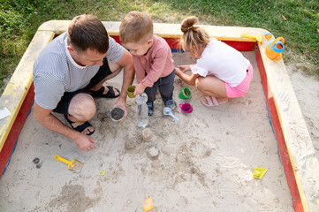Father enjoys playful moments with his children in a sandpit during a sunny afternoon in the park