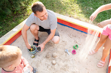 Father enjoys playtime with kids in sandbox on a sunny day in the backyard