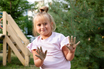 Little girl happily shows off her hands dirty with sand