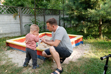 Сhild gets sand in his eyes while playing in the sandbox. The father helps his son