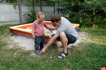 Father shows son that his shoes are full of sand after playing in the sandbox in a backyard