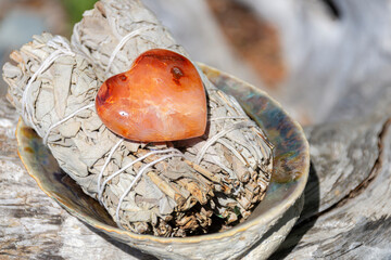 Heart shaped carnelian crystal and two white sage smudge sticks. 