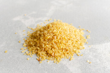 Pile of golden bulgur wheat grains on a light textured surface, showcasing the natural color and texture of this nutritious grain for culinary use and healthy recipes