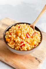 Bowl of cooked bulgur wheat mixed with colorful diced vegetables, including bell peppers and onions, served on a wooden cutting board, showcasing a healthy meal option