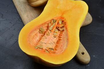 Freshly cut butternut squash revealing vibrant orange flesh and seeds, placed on a wooden cutting board against a dark textured background, showcasing healthy cooking ingredients