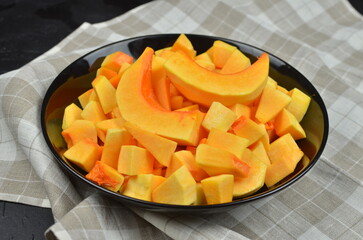 Freshly cut yellow and orange melon butternut squash pieces arranged in a black bowl on a textured cloth, showcasing vibrant colors and healthy snack options for summer enjoyment