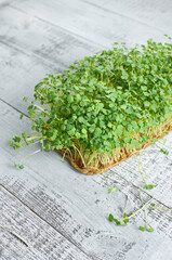 Fresh microgreens growing in a natural wooden tray on a rustic wooden surface, showcasing vibrant green leaves and roots, perfect for healthy culinary dishes and garnishes