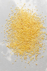 Yellow bulgur wheat seeds scattered on a light textured surface, showcasing their natural color and shape, ideal for culinary uses and healthy recipes in food photography