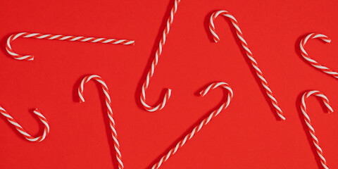 Red and white striped candy canes arranged on a bright red background. Festive minimal Christmas composition creating a joyful and sweet holiday mood, perfect for cards and seasonal design.