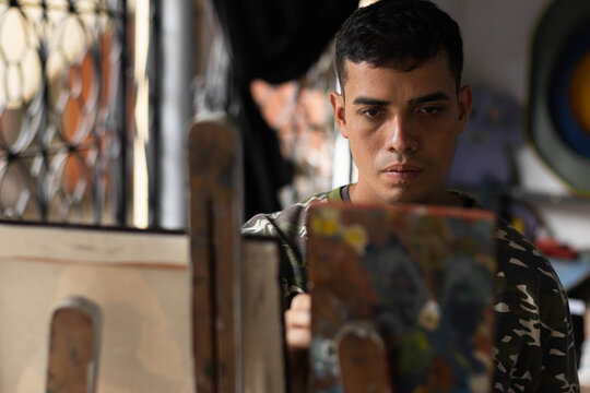 Young indigenous man concentrating while painting art in studio