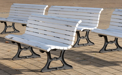 white wooden benches with metal legs arranged in rows on a paved area in soft afternoon sunlight